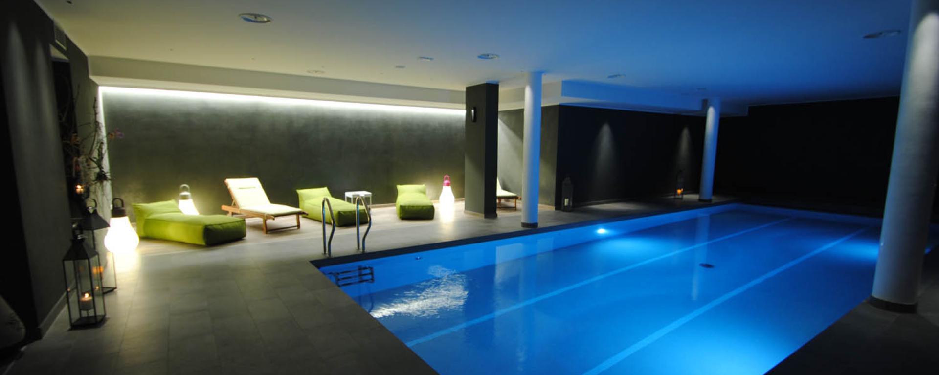 Piscina interna illuminata con lettini verdi e luci soffuse