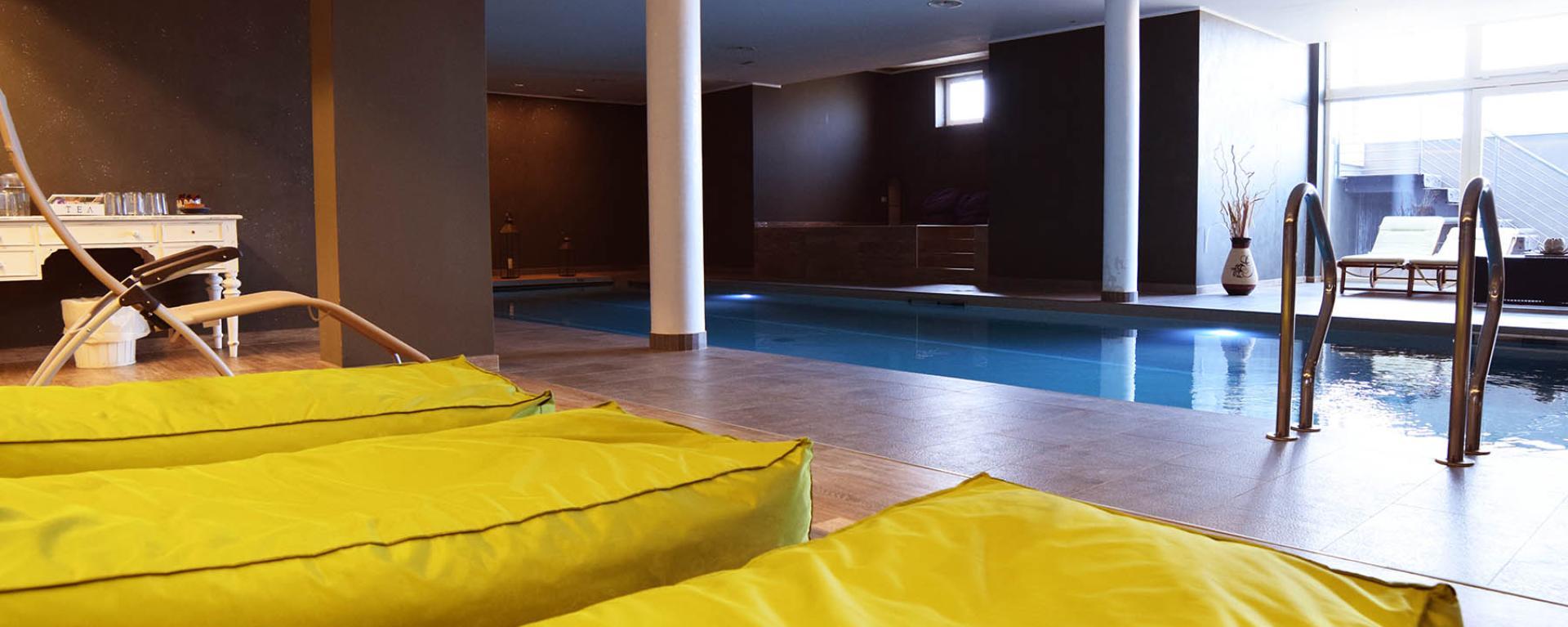Piscina interna elegante con lettini gialli e luce soffusa