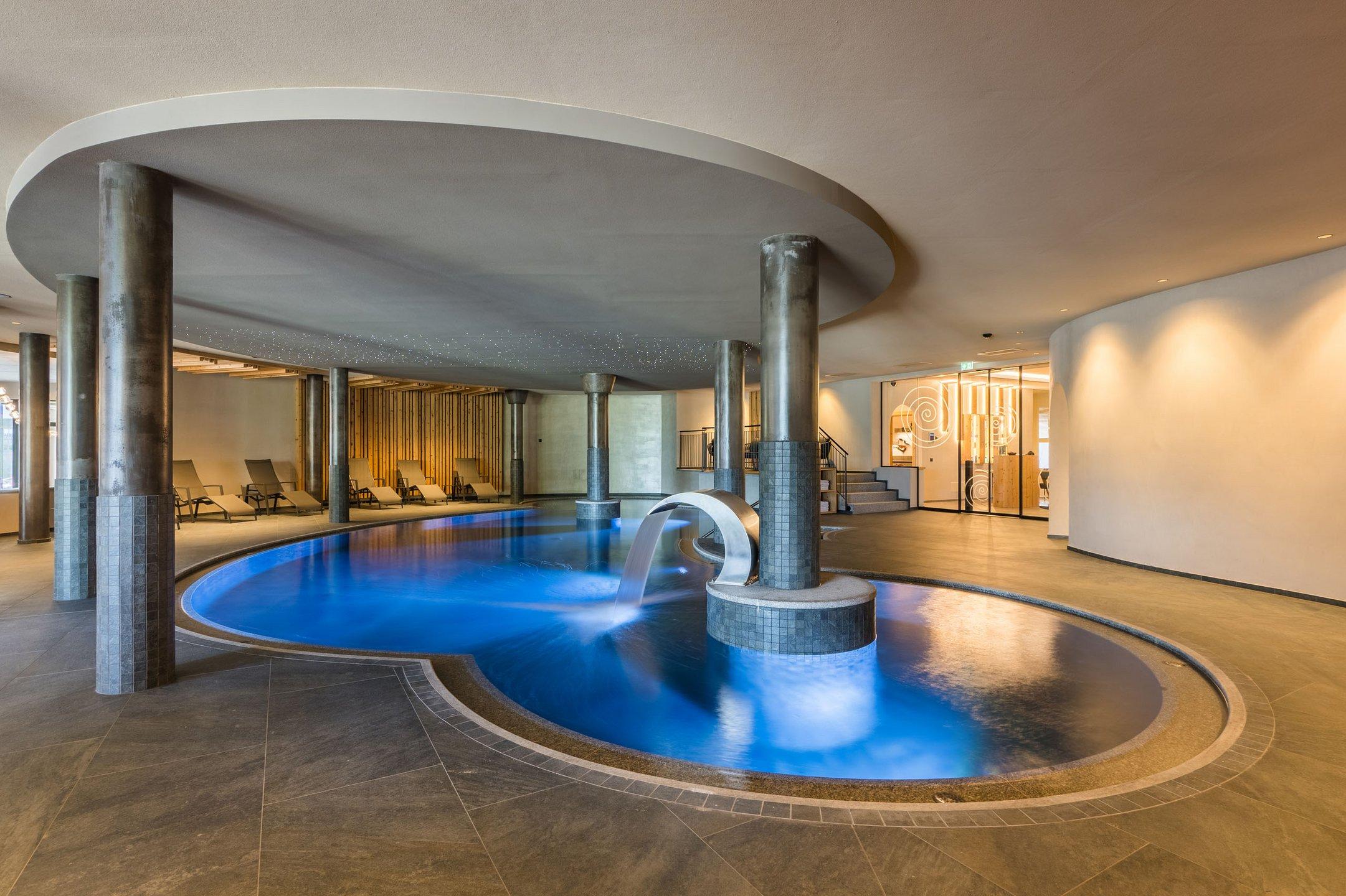 Piscina coperta con cascata e lettini nel centro benessere moderno