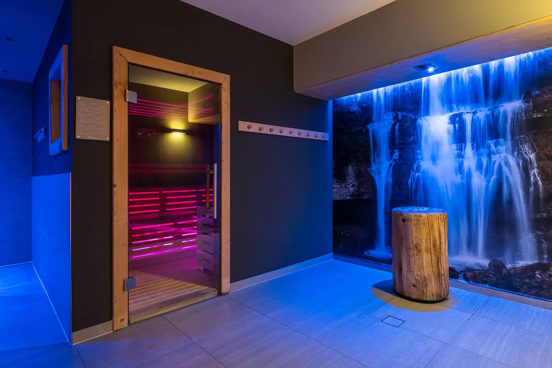 Porta di una sauna con luce colorata accanto a un'illustrazione di cascata illuminata di blu