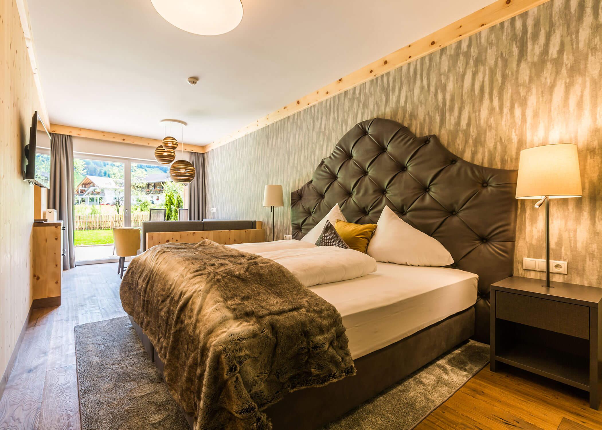 Camera da letto con testiera trapezoidale grande, biancheria da letto accogliente, lampade, TV e vista su giardino