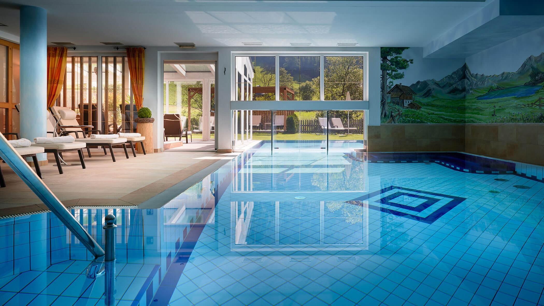 Piscina interna con lettini, grandi finestre e murales di montagne sulla parete
