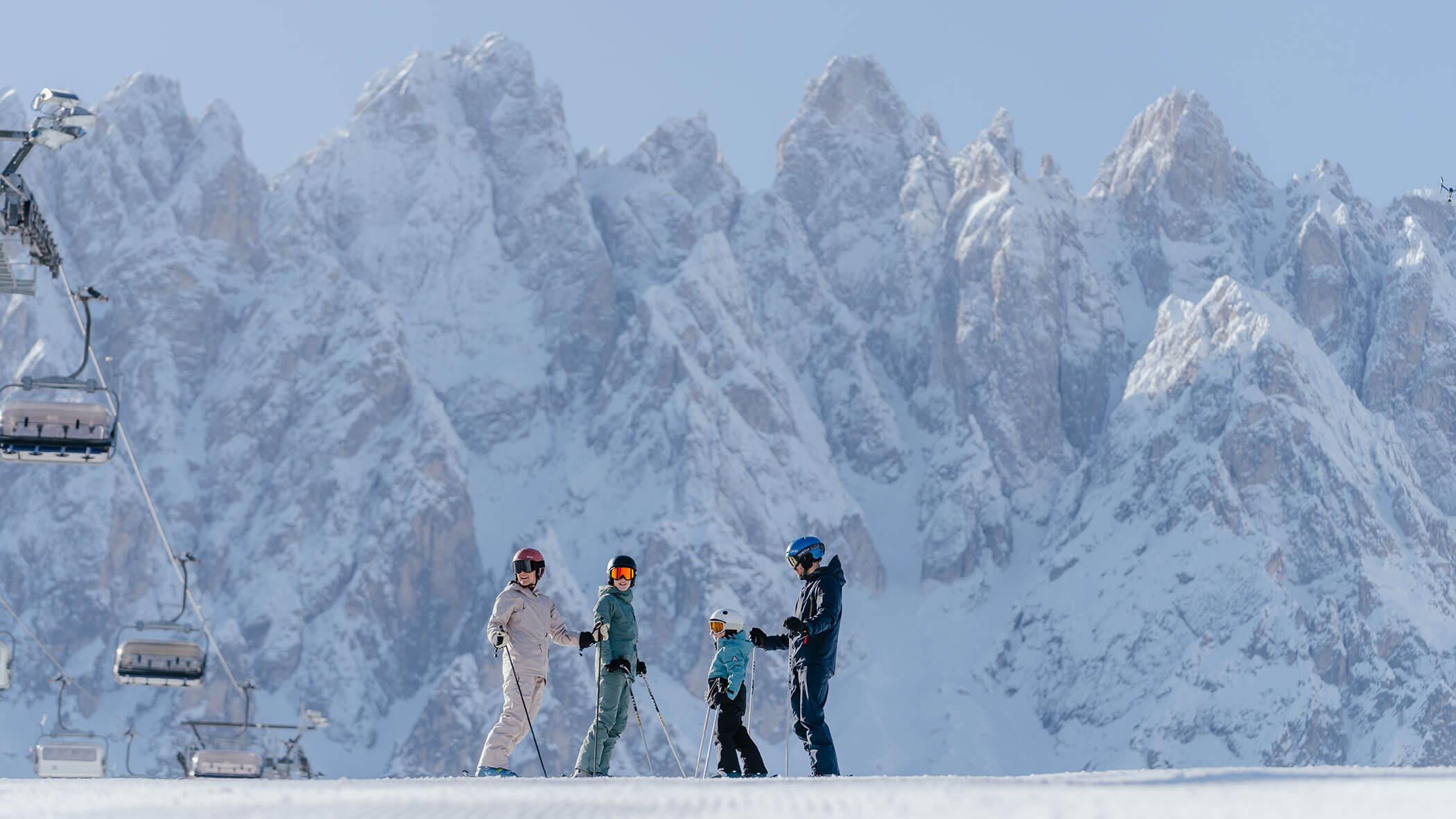 Quattro sciatori in attrezzatura sci su neve con montagne rocciose innevate sullo sfondo