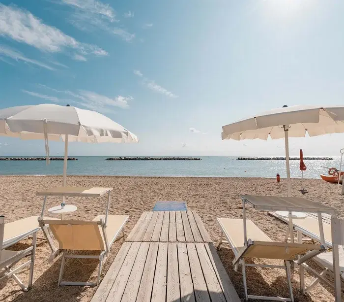 Lettini e ombrelloni beige su spiaggia sabbiosa con vista sul mare calmo