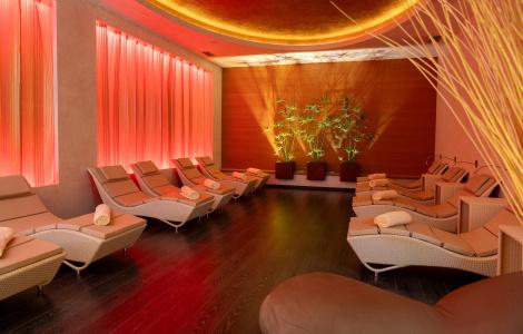 Sala relax con luci soffuse rosse, lettini accoglienti e piante decorative in atmosfera serena
