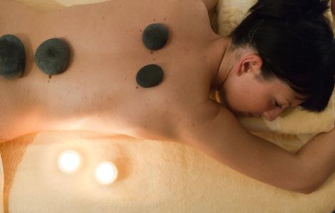 Donna rilassata con pietre calde sulla schiena, candele accese creano atmosfera serena