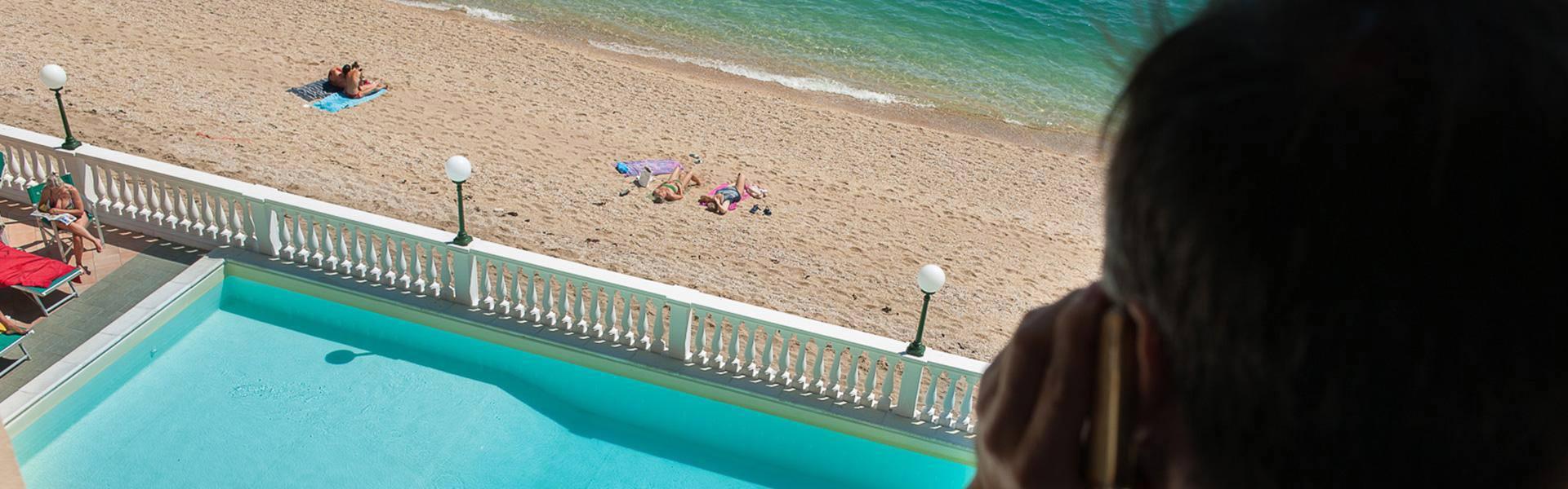 Vista dalla terrazza: piscina, spiaggia e mare, persona al telefono