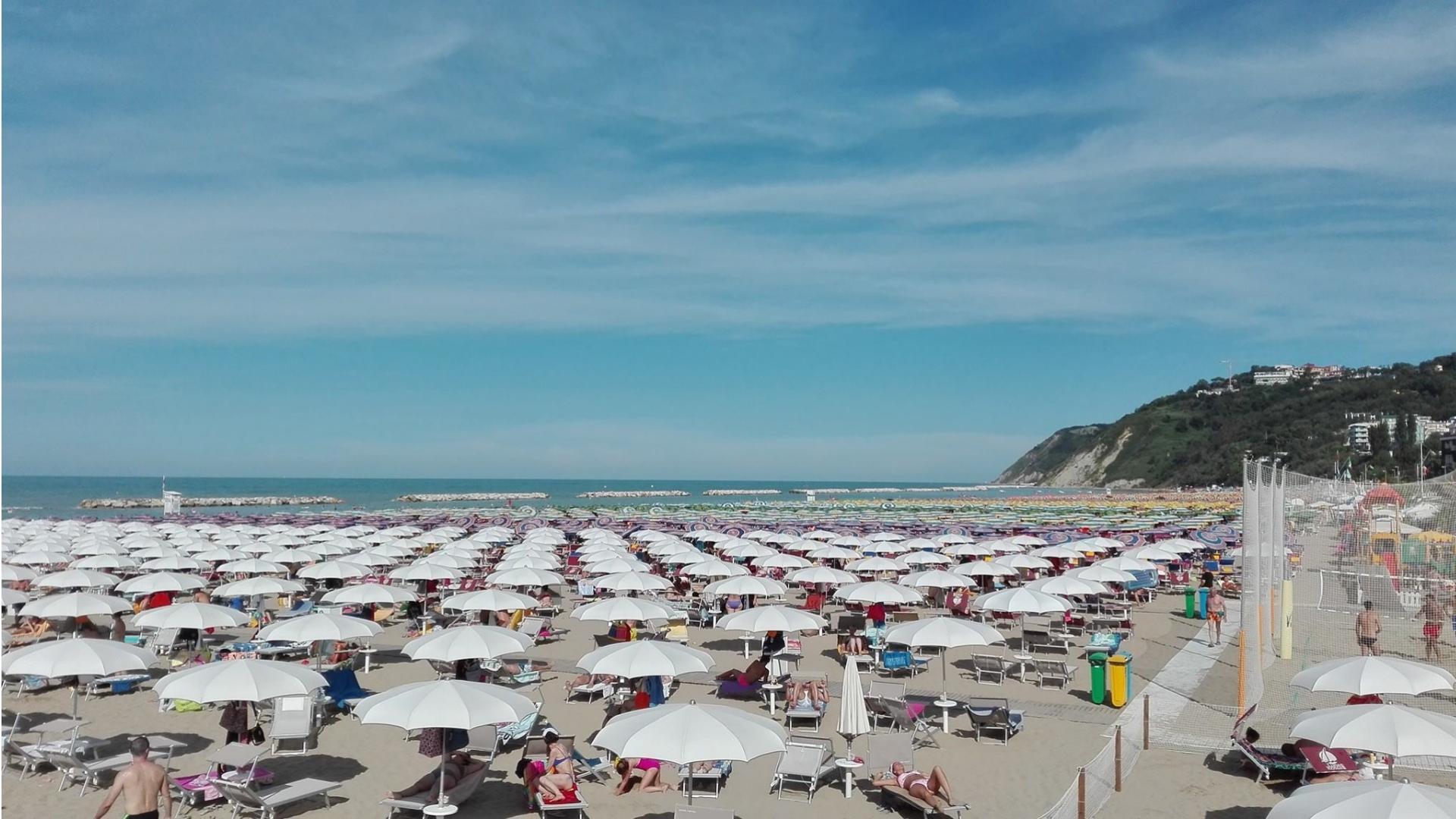 Spiaggia affollata con ombrelloni bianchi e mare calmo