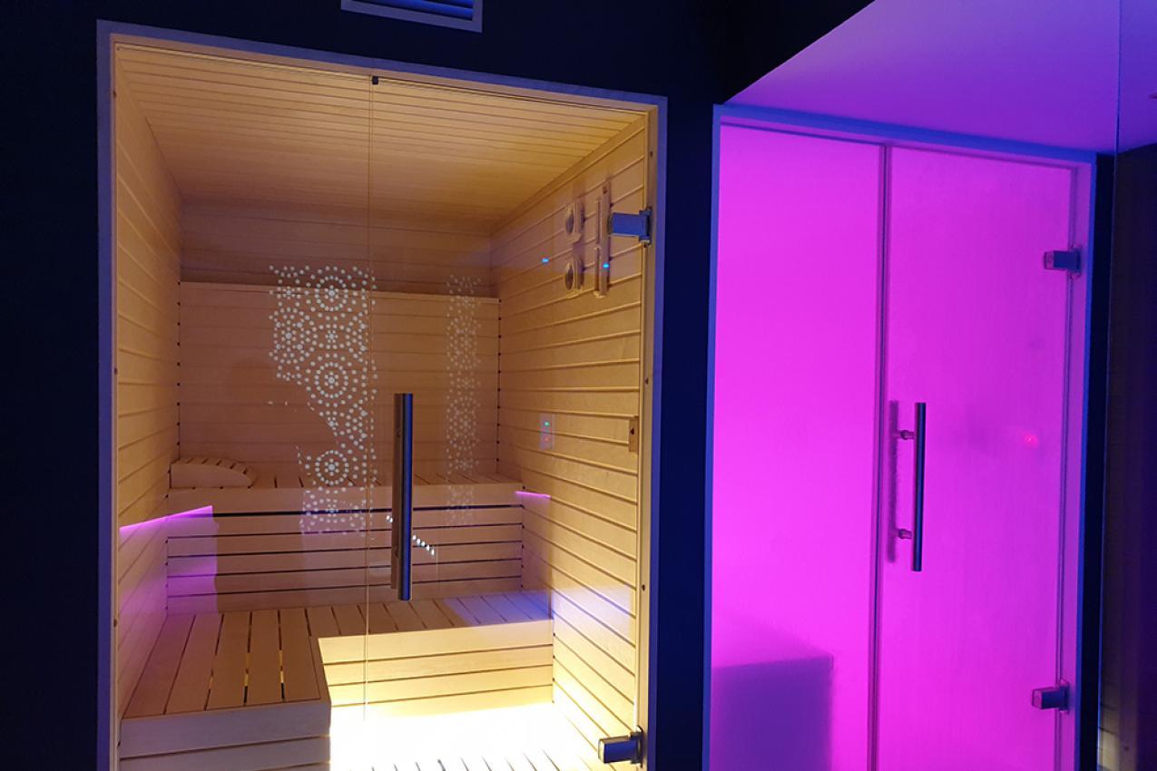 Sauna moderna con illuminazione colorata e porta in vetro