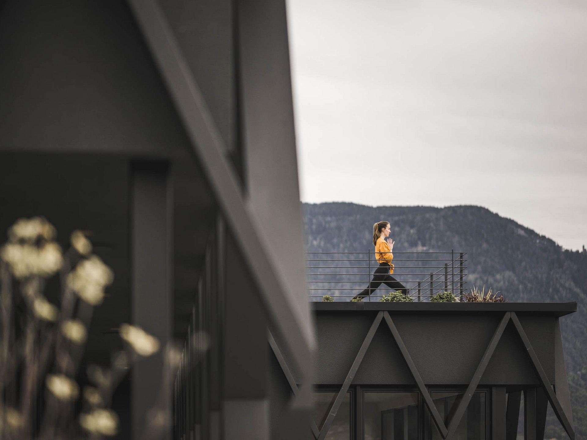 Donna esegue esercizio yoga su terrazza con vista montagna