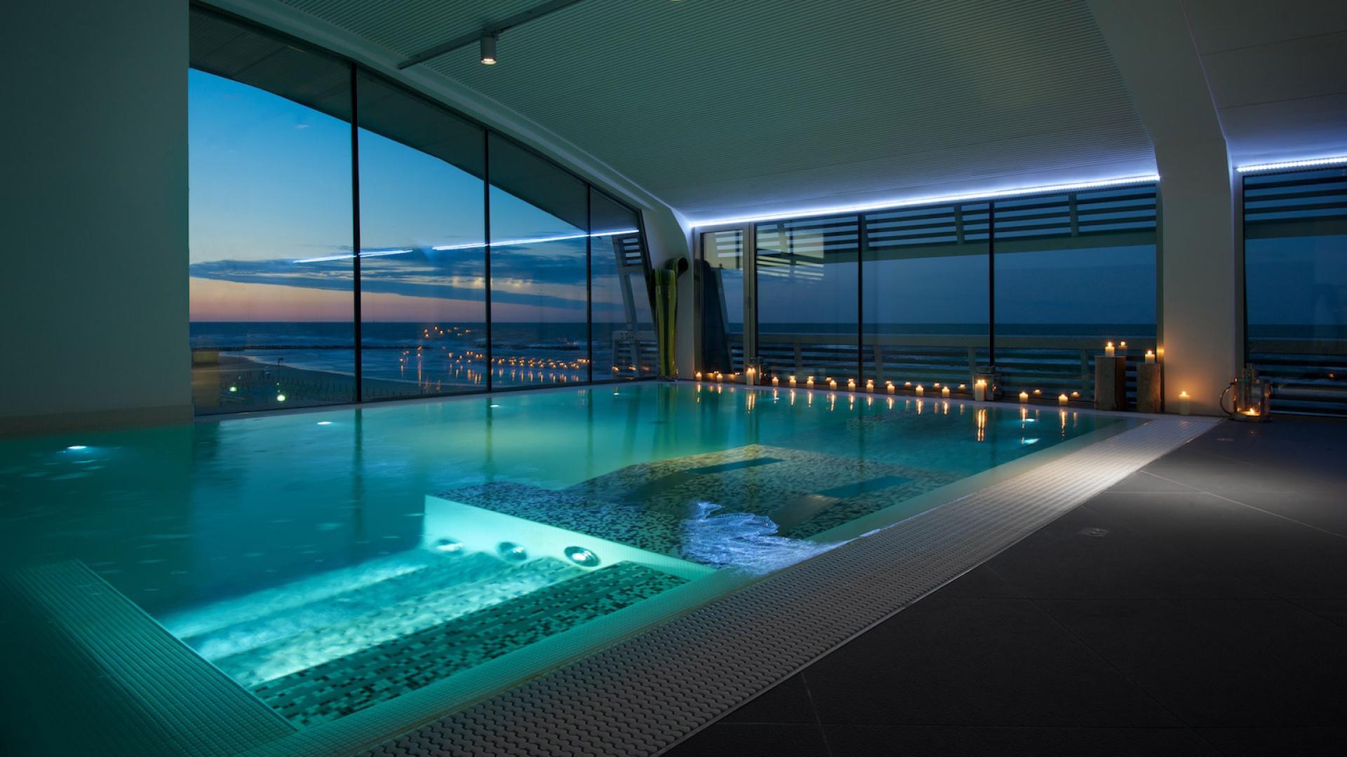 Piscina interna elegante al tramonto, luci soffuse e vista mare
